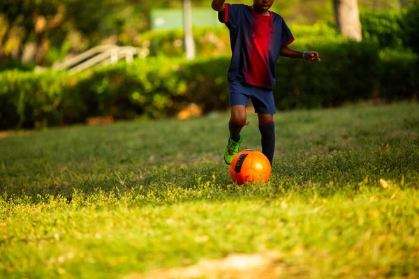 Primer plano de las piernas del adolescente con una pelota en el campo de fútbol. Recortado tiro de fútbol jugador de entrenamiento en el campo de césped artificial —  Fotos de Stock