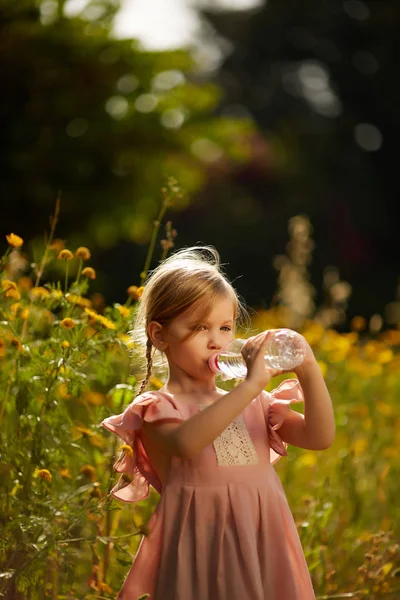 幼児の女の子はペットボトルから水を飲むです。子供の園芸。子供は、裏庭の花を収集します。子供たちは庭での作業します。子供たちは、植物を世話します。最初の春 flo — ストック写真