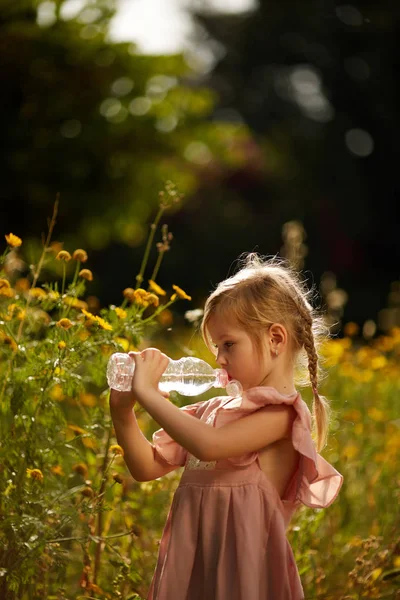 Roztomilá dívka s lahví vody v květu pole — Stock fotografie