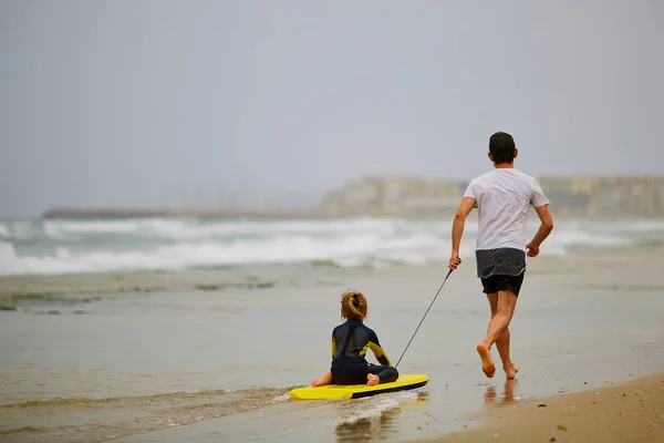 Papa rollt kleine Tochter auf Surfbrett — Stockfoto