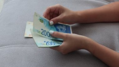 İsrail parası sayan bir kıza yaklaş. 200 İsrail şekeli banknot saymak - büyük miktarda paraya yakın.