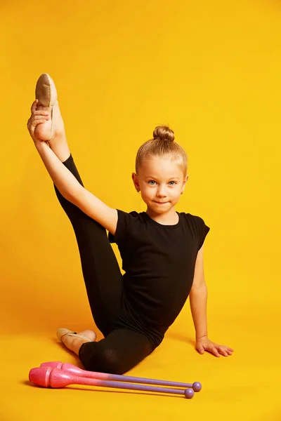 Κορίτσι γυμναστής προπονείται με γυμναστικές λέσχες σε κίτρινο φόντο. παιδικά επαγγελματικά αθλήματα. Όμορφη έφηβη που κάνει ρυθμικές ασκήσεις γυμναστικής — Φωτογραφία Αρχείου