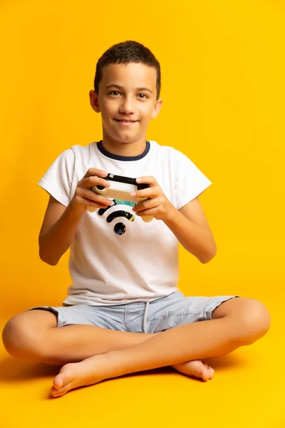 Ребенок с помощью видеоигры. Ребенок с джокером играет в игру на желтом фоне — стоковое фото