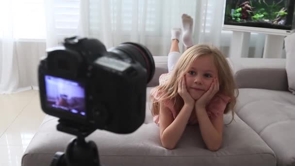 Graciosa niña sonriendo mirando a la cámara en casa, lindo niño hablando con webcam haciendo videollamada en línea o grabación vlog divertirse, niño preescolar con cara bonita acostado en el sofá — Vídeo de stock