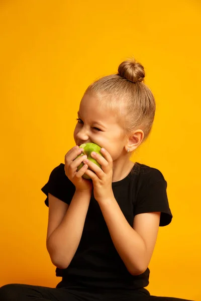 El retrato de una niña muerde manzana. Pretty girl bits manzana fresca aislada sobre un fondo amarillo —  Fotos de Stock
