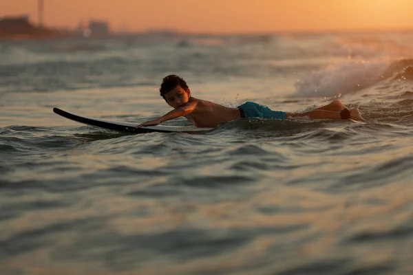 行動中のサーファー。夕暮れ時や日の出時に波に乗る少年 — ストック写真