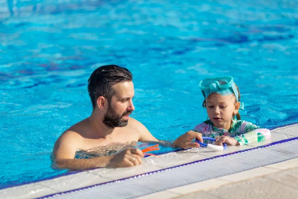 Père apprend aux filles à nager dans la piscine. Père heureux apprenant à sa petite fille à nager. Enfant actif et heureux apprenant à nager. Petite fille dans une piscine — Photo