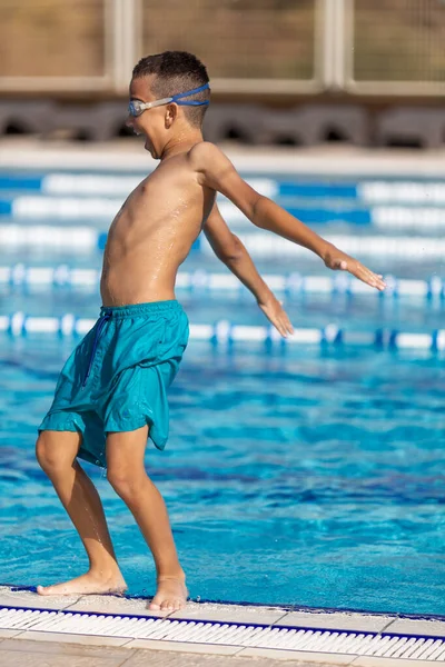 Мальчик играет в открытом бассейне, падает в воду, летние развлечения для детей — стоковое фото