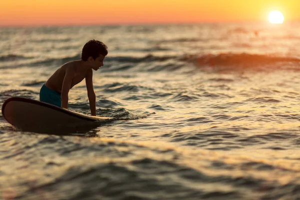 Silhueta de uma criança com uma prancha de surf no desfoque nas horas da noite — Fotografia de Stock