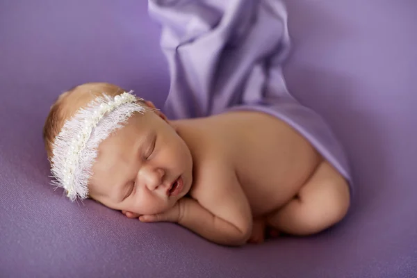 Niña recién nacida con un vendaje en la cabeza duerme tranquilamente sobre un fondo lila cubierto con tela de seda . —  Fotos de Stock