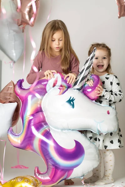 Two little girls play with a big unicorn balloon surrounded by balloons — Stock Photo, Image