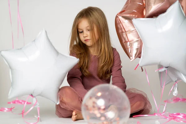 Retrato de niña rubia caucásica triste con globos de colores sobre fondo blanco — Foto de Stock