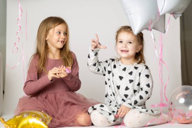 İki kız kardeş bir fotoğraf stüdyosunda yerde oynuyorlar.