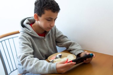 Çocuk oyun yüzünden dikkati dağınık yiyor. Pirinç yiyen ve internette sörf yapan ya da konsolda oyun oynayan bir çocuk.
