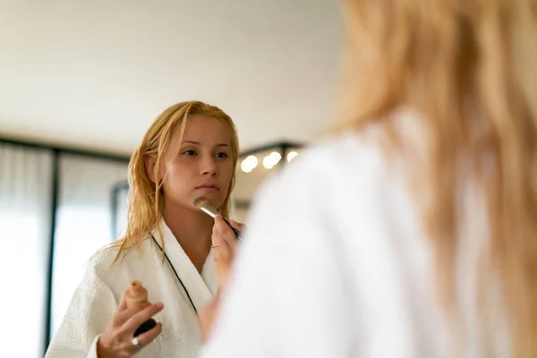 Потрясающая женщина стоит перед зеркалом и наносит макияж. — стоковое фото