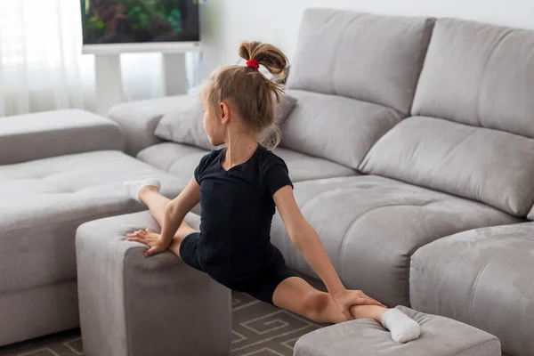 Petite fille mignonne pratique la gymnastique à la maison. Formation en ligne. S'étirer, ficelle. En quarantaine. Reste à la maison. — Photo