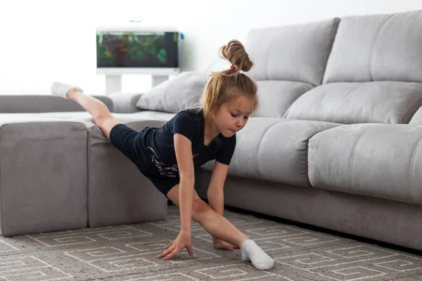 Выполняем полную бечевку. Эластичная маленькая девочка делает гимнастику на мебели в гостиной при ярком дневном свете — стоковое фото