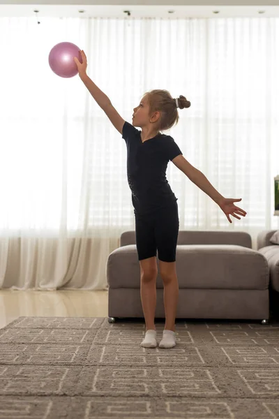 Jeune fille aux yeux bleus fait de la gymnastique rythmique dans un body noir, joue avec une balle rose sur la maison — Photo