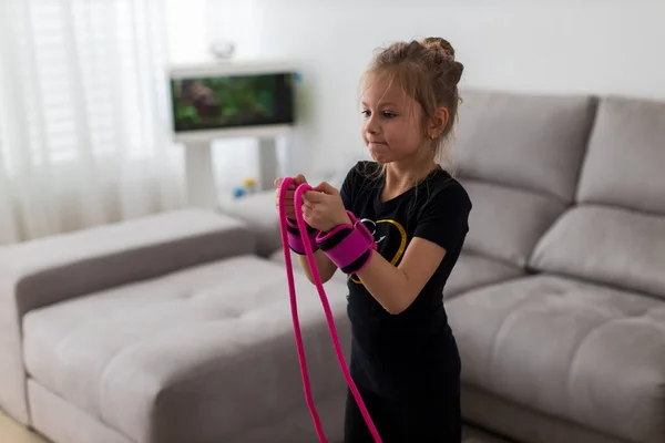 Little cute girl is practicing gymnastics at home. Online training. Jumping rope. Quarantine. Stay at home