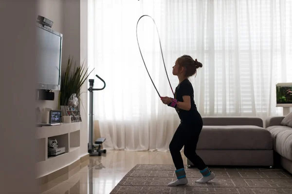 Happy little girl jumping over the rope at home during the isolation. The bright sun illuminates the room