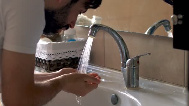 Banyoda sakallı bir adam var. Yüzünü yıkar. Aynadaki yansıma. Kabarık saçlı. Hijyen. Antibakteriyel tedavi — Stok video