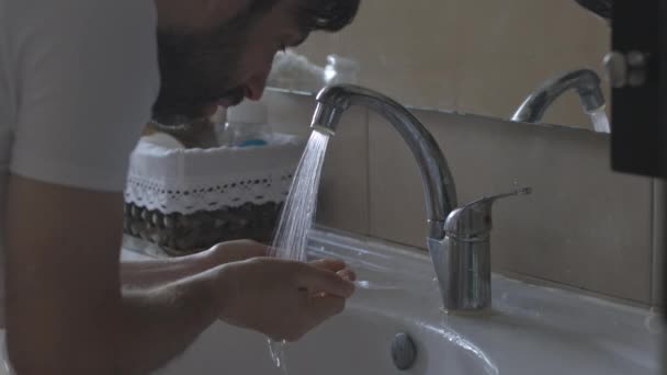Muž s vousy v koupelně. Umyje obličej. Odraz v zrcadle. neutrální barevné video — Stock video