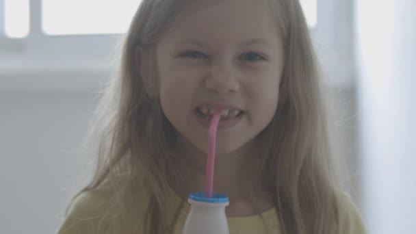 Little girl is drinking milk. child drinks milk from a small bottle through a pink tubule indoors lifestyle morning breakfast — Stock Video