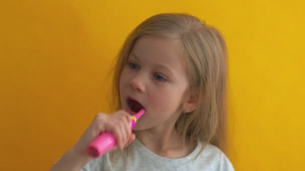 Charmantes kleines Mädchen im grauen T-Shirt, das Zähne putzt, mit bunten Kinderzahnbürsten, die in die Kamera schauen — Stockvideo