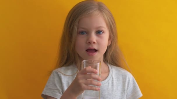 Attraktives kleines Mädchen mit einem Glas Wasser auf gelbem Hintergrund — Stockvideo