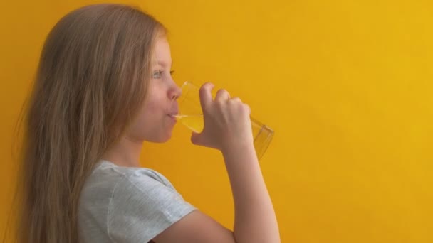 Όμορφο κορίτσι πίνει καθαρό νερό από γυαλί σε κίτρινο φόντο. Κοντινό πλάνο πορτρέτο του παιδιού με ένα ποτήρι νερό — Αρχείο Βίντεο