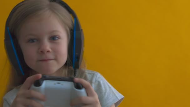 Grappig meisje in groot verband op een gele achtergrond speelt met de hulp van joystick vol vertrouwen concentreren op het spel — Stockvideo