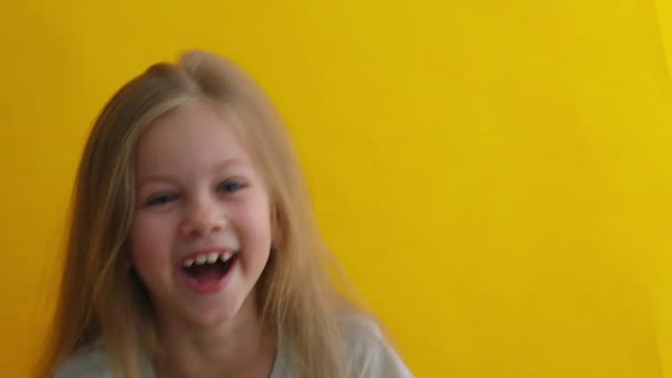 Lykkelig pige med blondt hår og blå øjne griner højt, moret af sjov joke, nyder positive følelser. indendørs studie skudt isoleret på gul baggrund – Stock-video