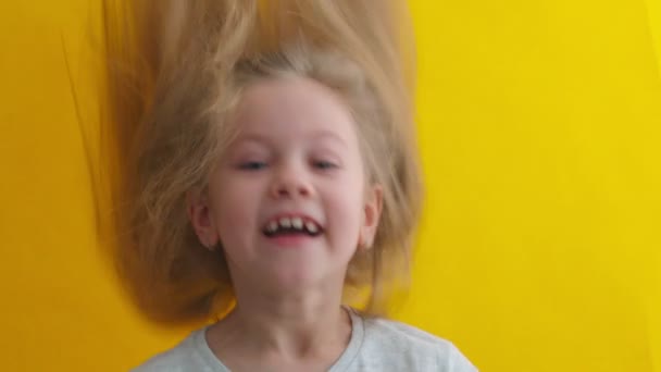 Una niña linda y graciosa agitando la cabeza. Hermosa niña de siete años. Niño rubio lindo. ojos azules. De cerca. fondo amarillo — Vídeos de Stock