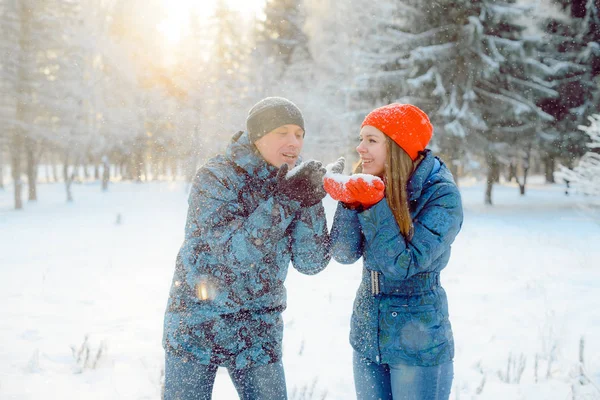 Glada och vackra unga par, en tjej och en ung man vandrar i den frostiga vintern parken leker med snön, blås snö med det. — Stockfoto