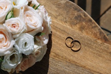 Alyanslar ve gelinin beyaz gül buketi masanın üstünde..