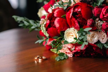 Gelinin buketi kırmızı güller ve alyanslar masanın üstünde.