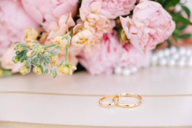 Gelinin pembe şakayık buketinin önündeki masanın üzerinde iki ince altın alyans var.