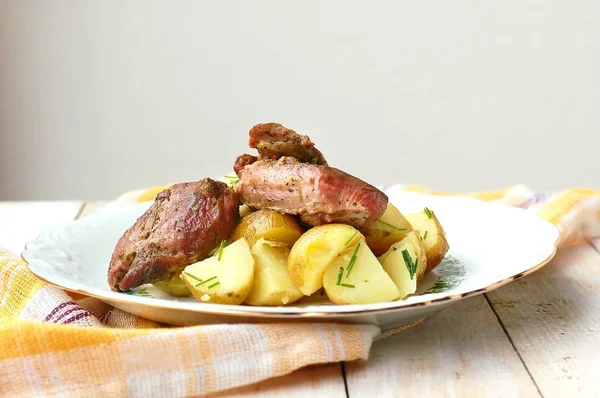 Carne de peru assada com pimenta preta e tomilho fresco, batatas de primavera com cebolinha em placa branca e madeira Imagem De Stock