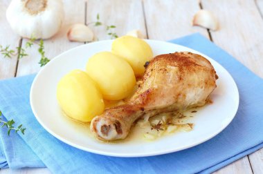 Taze sarımsak, kekik ve ahşap zemin üzerine mavi kumaş üzerine beyaz tabakta patates ile kavrulmuş tavuk