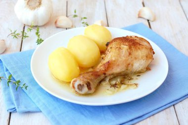 Taze sarımsak, kekik ve ahşap zemin üzerine mavi kumaş üzerine beyaz tabakta patates ile kavrulmuş tavuk