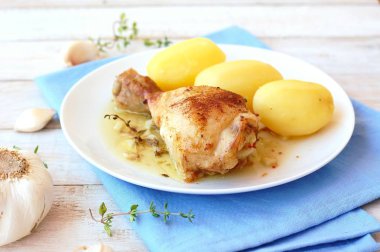 Taze sarımsak, kekik ve ahşap zemin üzerine mavi kumaş üzerine beyaz tabakta patates ile kavrulmuş tavuk