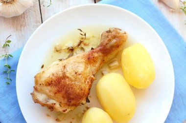 Taze sarımsak, kekik ve ahşap zemin üzerine mavi kumaş üzerine beyaz tabakta patates ile kavrulmuş tavuk