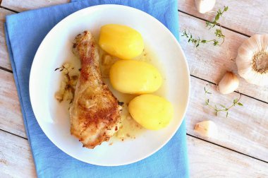 Taze sarımsak, kekik ve ahşap zemin üzerine mavi kumaş üzerine beyaz tabakta patates ile kavrulmuş tavuk