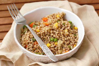 Sağlıklı çek vegan yemek, havuç, Mısır, bezelye, taze fasulye ve soğan kahverengi kumaş üzerine çatal ile beyaz kase ile buğday