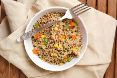 Sağlıklı çek vegan yemek, havuç, Mısır, bezelye, taze fasulye ve soğan kahverengi kumaş üzerine çatal ile beyaz kase ile buğday