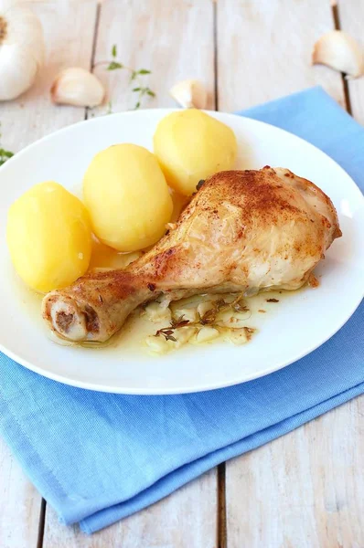 Roasted chicken with fresh garlic, thyme and potatoes on white plate on blue cloth on wooden background — Stock Photo, Image