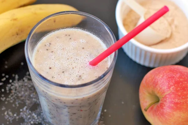 Healthy fresh smoothie drink from red apple, banana chia seeds and plant protein powder in the glass with straw