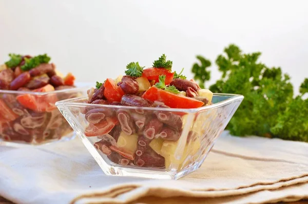 Frischer gesunder veganer Salat mit roten Bohnen, Tomaten, Paprika, Paprika und Petersilie in Glasschale auf braunem Tuch auf Holzgrund — Stockfoto