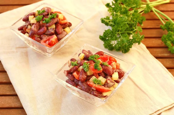 Frischer gesunder veganer Salat mit roten Bohnen, Tomaten, Paprika, Paprika und Petersilie in Glasschale auf braunem Tuch auf Holzgrund — Stockfoto