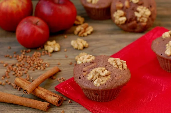 Gluten free muffins from buckwheat flour, apple, cinnamon and walnuts on red cloth on brown wooden table with black background